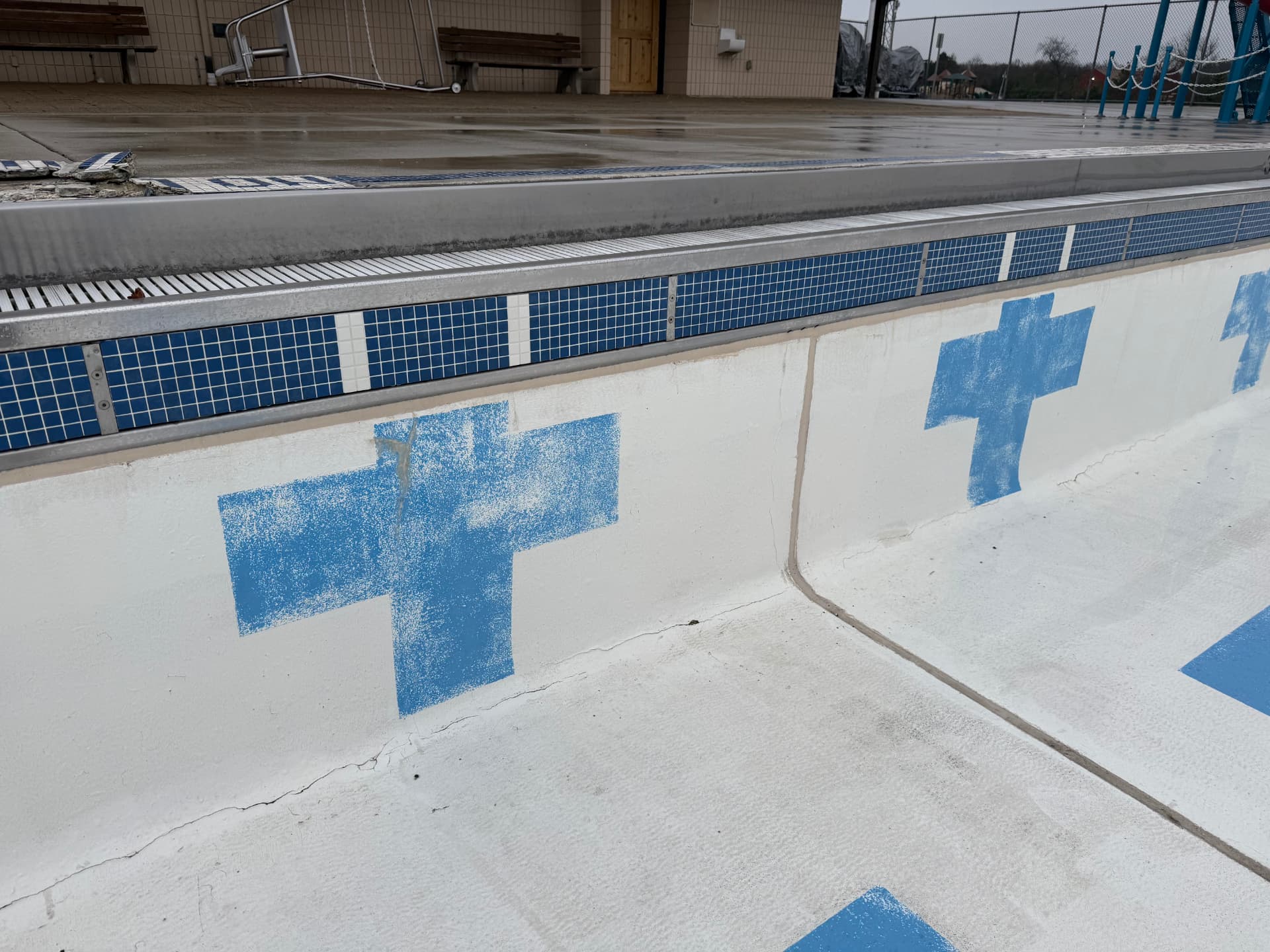 Drained commercial pool basin wall with blue waterline tile and steel coping